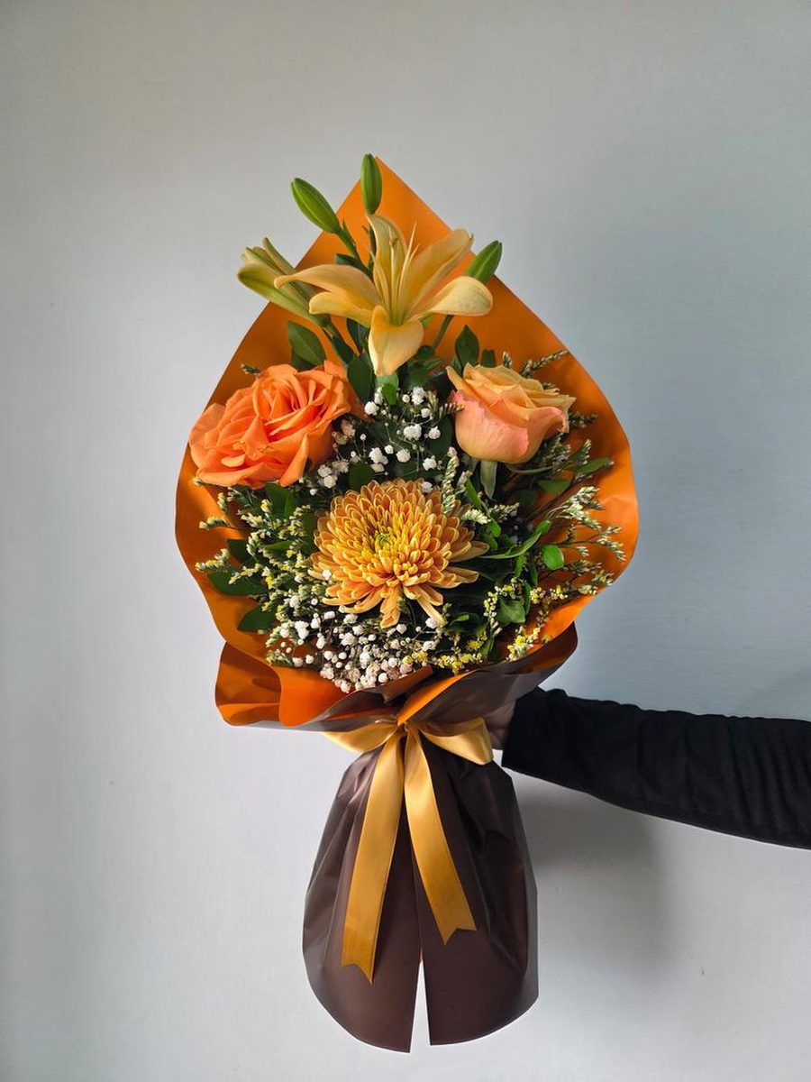 Ramo en tonos naranja con lirio, rosas y crisantemo en papel naranja y chocolate