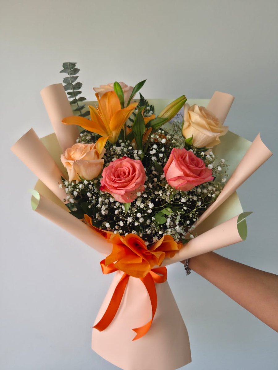 Ramo de lirio naranja, rosas durazno y rosadas con paniculata y eucalipto en papel melocotón con lazo naranja