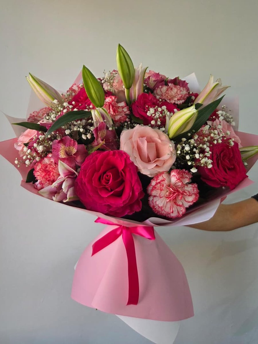 Ramo de rosas fucsia, claveles jaspeados, lirios rosados y astromelias con paniculata en papel rosa con lazo fucsia
