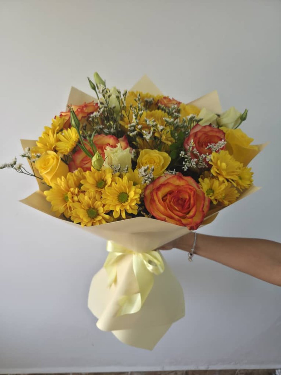 Ramo de crisantemos amarillos, rosas naranja y lisianthus blanco en papel crema con lazo crema