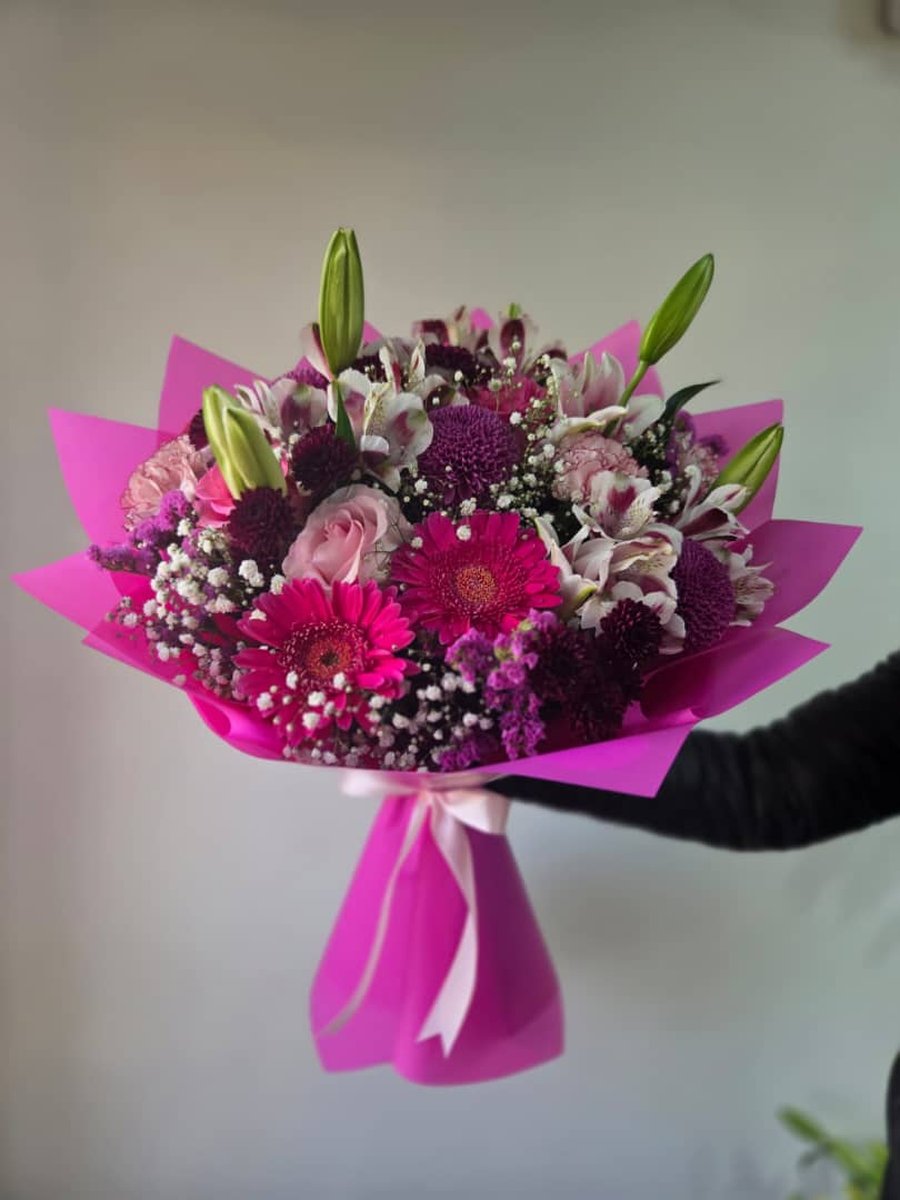 Ramo de gerberas fucsia, crisantemos morados, lirios y rosas rosadas con paniculata en papel fucsia con lazo rosa