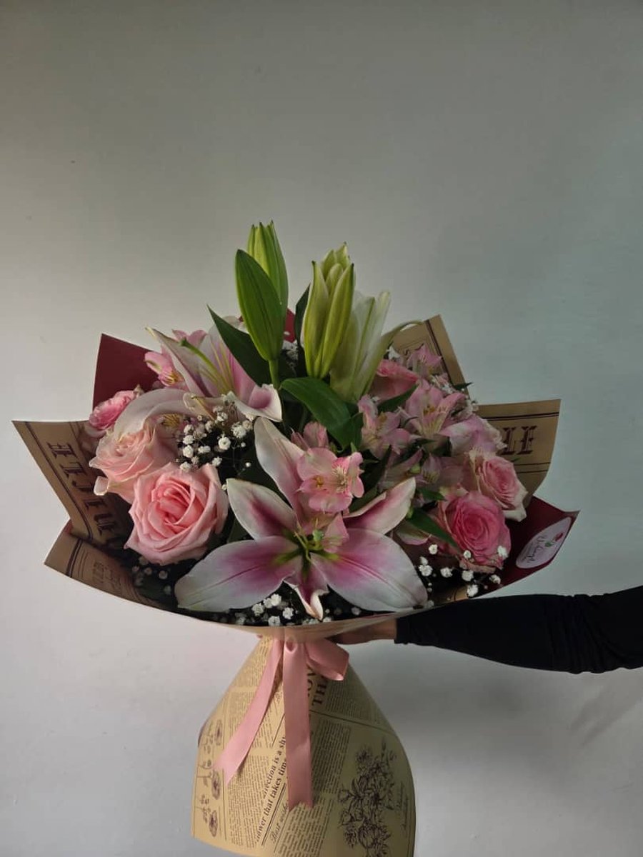 Ramo de lirios rosados abiertos, rosas rosadas y astromelias con paniculata en papel tipo periódico con lazo rosa